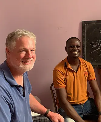 A smiling Maryknoll Lay Missioner, Mike, sits with a Haitian also smiling.