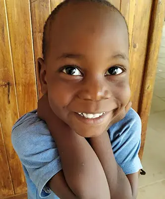 Close-up of a smiling Tanzanian child holding his hands close to his face.