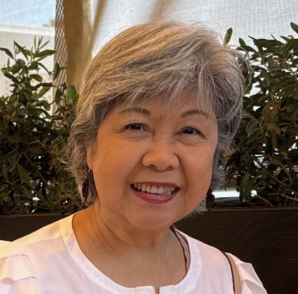 Maryknoll Lay Missioner, Gaby Hernandez, stands in front of the American, Bolivia, Vatican, and El Salvador flags signifying her connection to MKLM in America, her home nation of El Salvador, the Catholic connection from the Vatican, and her place of mission in Bolivia.