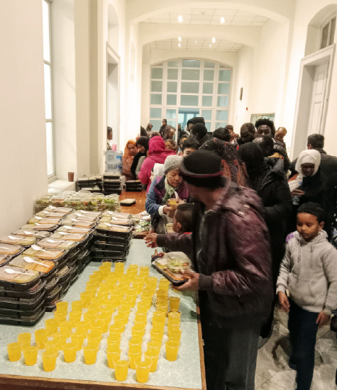 Migrants in Lebanon approach a table of prepared meals and cups of juice