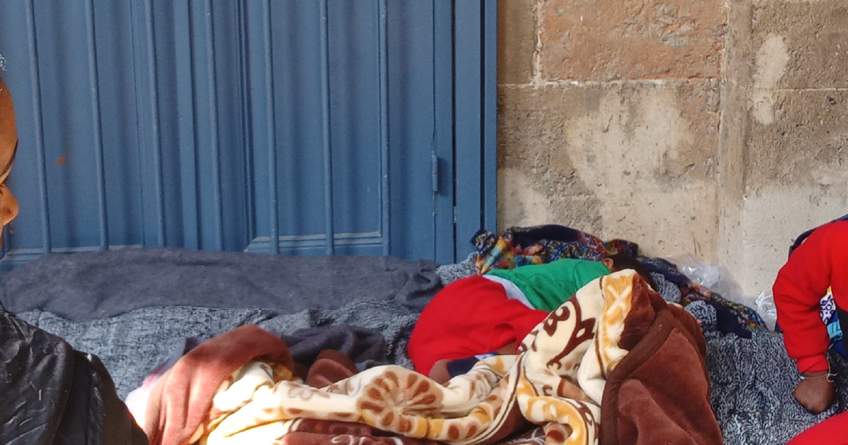 Migrants sleep on the ground in front of the parish entryway, waiting.