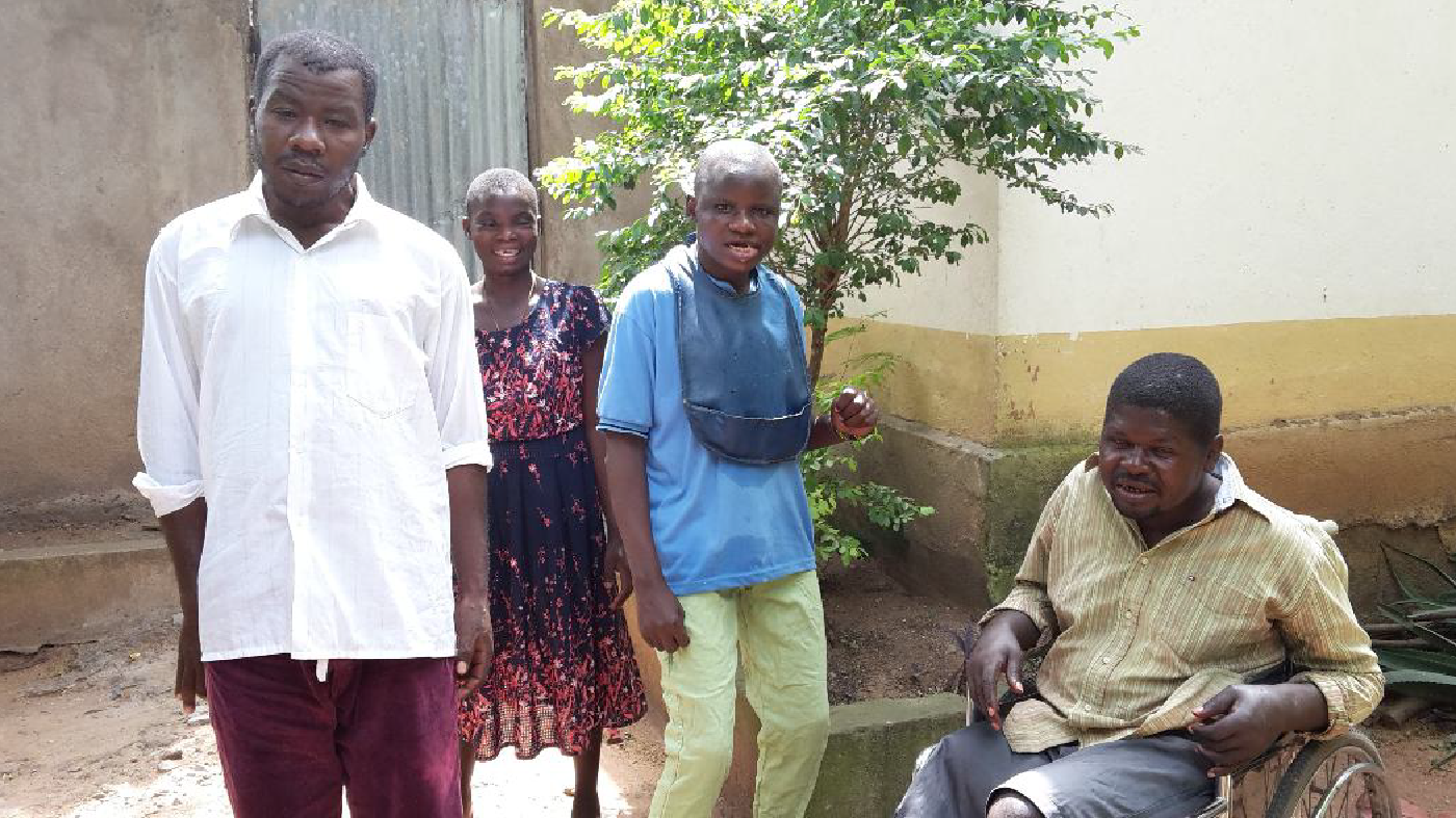 4 individuals with a visible disability pose for the camera: A man in a wheelchair, next to a young adult male and young adult female with an elder gentleman.