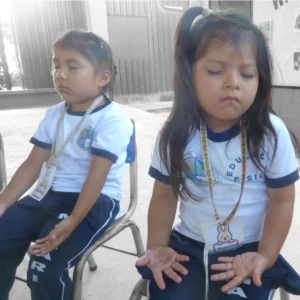 Two young girls sit with their eyes closed and their hands in an open position resting on their laps during a moment of prayer.