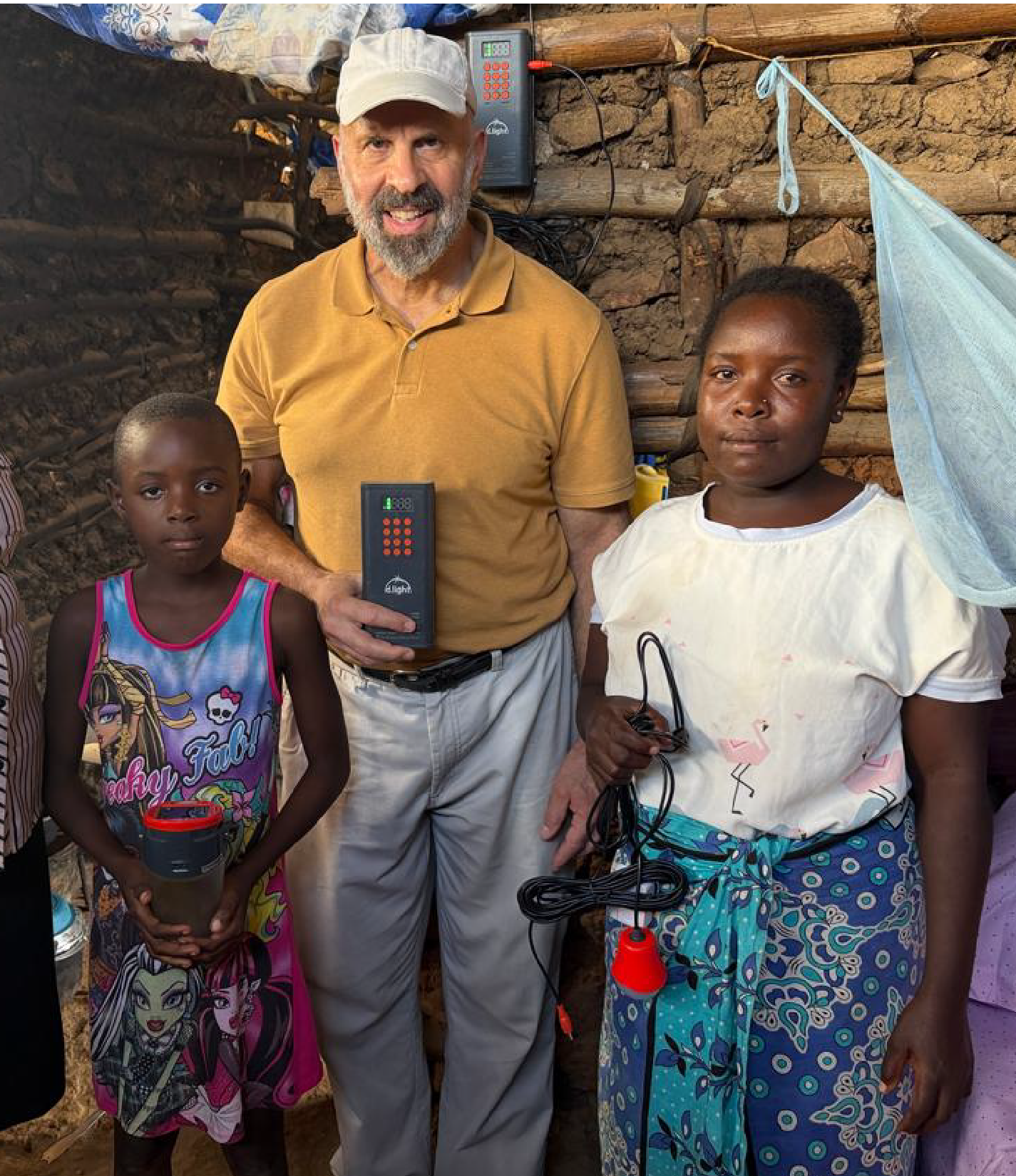 Maryknoll Lay Missioner Rich Tarro poses with a mother and a child in a Monster High nightgown. All three hold different supplies for the solar panel they installed inside the home.