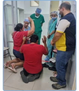 A group of people in a hospital hallway, 2 have their hands up in prayer as 3 doctors bow their heads and Juan Gomez watches.