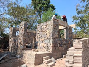 Two workers, work on the wooden forms around a window cut-out of an all stone structure.